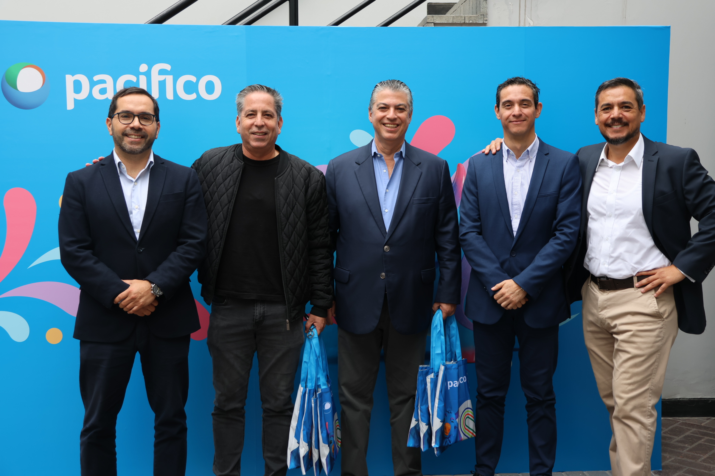 Fotografía de participantes junto al panel institucional de Pacífico Seguros
